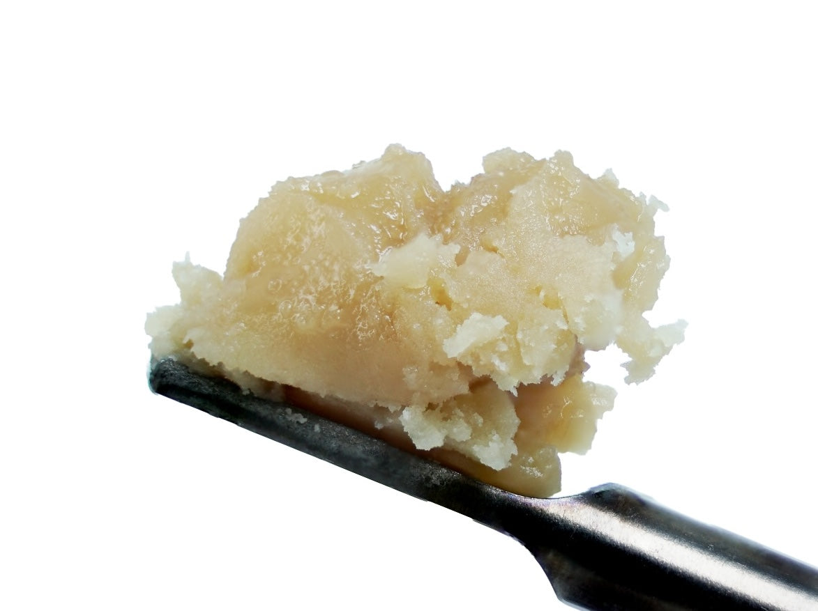 A close-up of a metal spoon holding a pale, crumbly, beige substance—StrawGuava THCa Hash Rosin by roz from frasier—set against a white background, ideal for those seeking chronic pain relief.